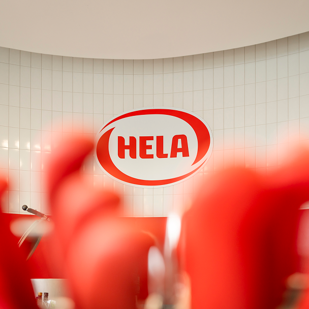 HELA-Logo an einer Wand hinter roten, unscharfen Formen