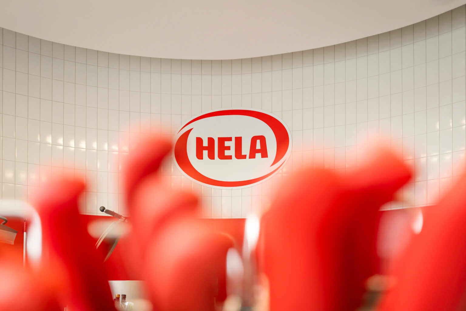 Logotipo de HELA en una pared detrás de formas rojas desenfocadas