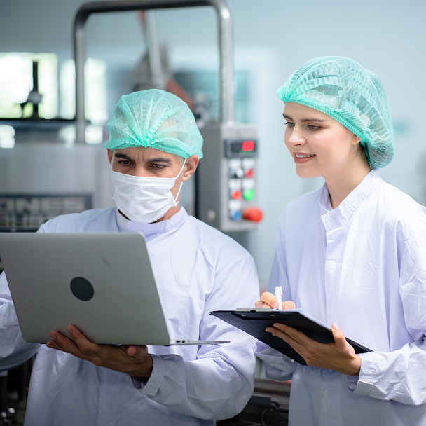 Zwei Mitarbeitende in Schutzkleidung prüfen Daten auf einem Laptop